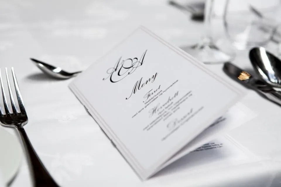 A printed wedding card with decorative lettering on a laid table