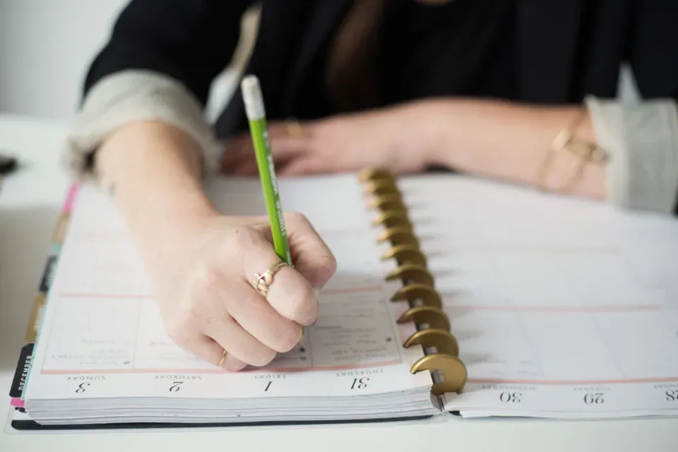 A hand writing a to-do list in a ring-bound planner
