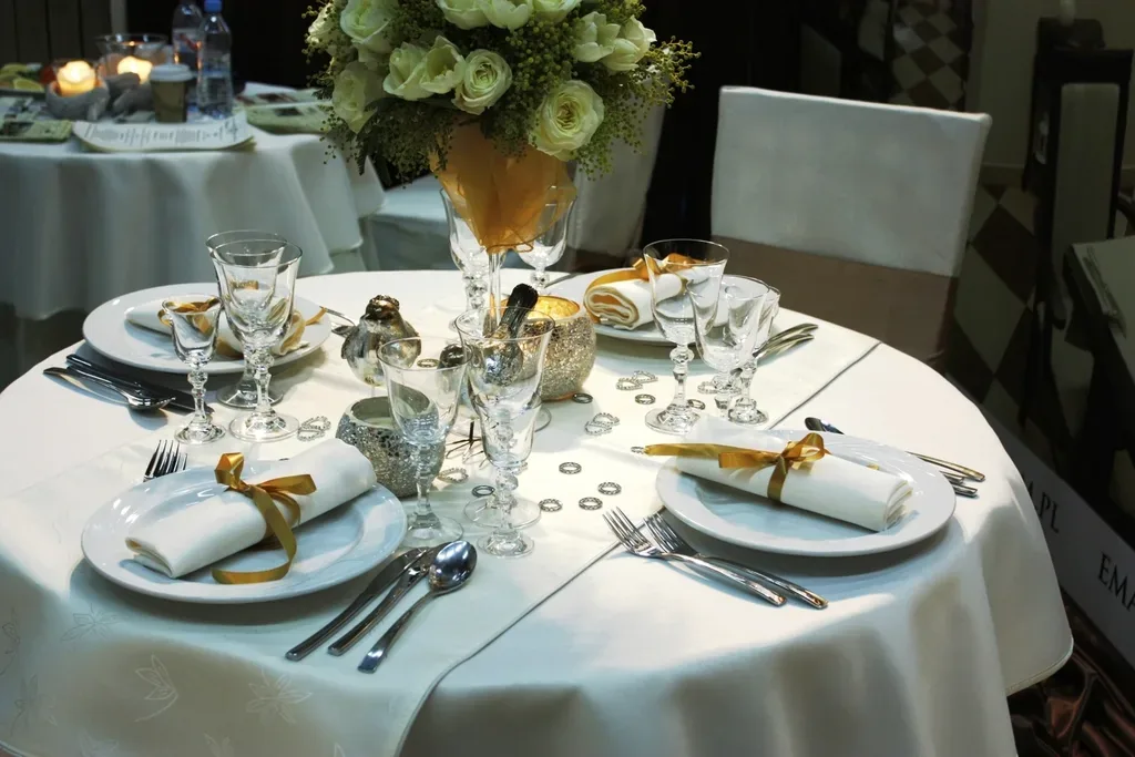 A round wedding table with place settings, napkins tied with gold ribbon and flowers